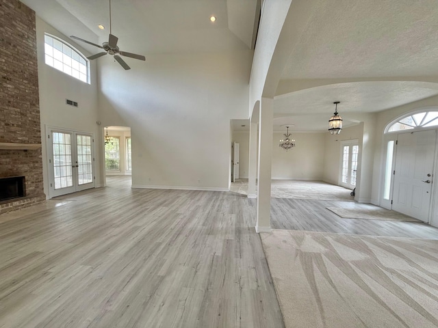unfurnished living room with visible vents, baseboards, light wood-style floors, a fireplace, and ceiling fan with notable chandelier