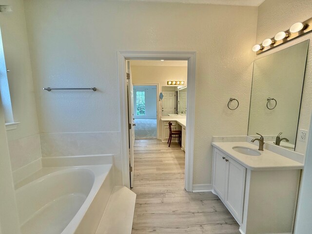 full bathroom featuring a textured wall, vanity, a garden tub, and wood finished floors