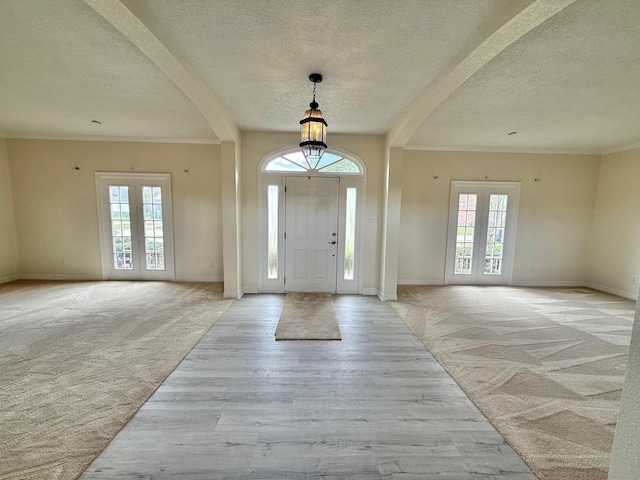 entrance foyer featuring light wood-style floors, light colored carpet, crown molding, and baseboards