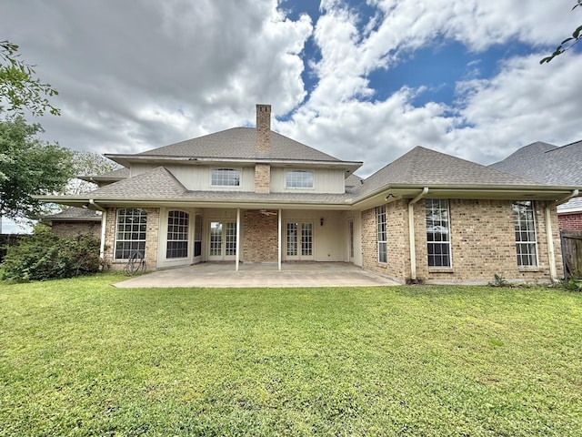 rear view of property with a patio, roof with shingles, french doors, brick siding, and a lawn