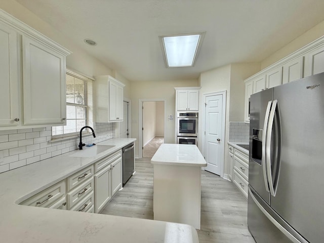 kitchen with tasteful backsplash, light wood-style flooring, white cabinetry, appliances with stainless steel finishes, and a sink