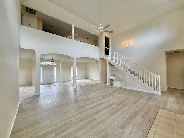 unfurnished living room with a towering ceiling, light wood-type flooring, stairway, a ceiling fan, and arched walkways