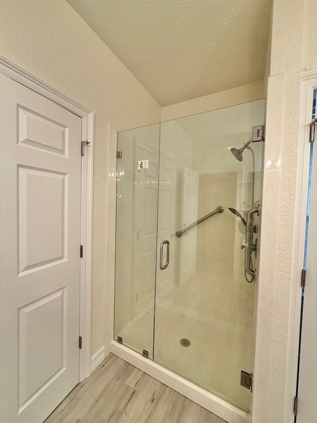 bathroom with a textured wall, a textured ceiling, a stall shower, and wood finished floors