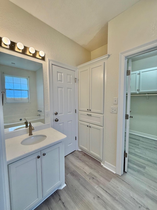 full bathroom featuring a bathing tub, a textured ceiling, wood finished floors, a textured wall, and baseboards