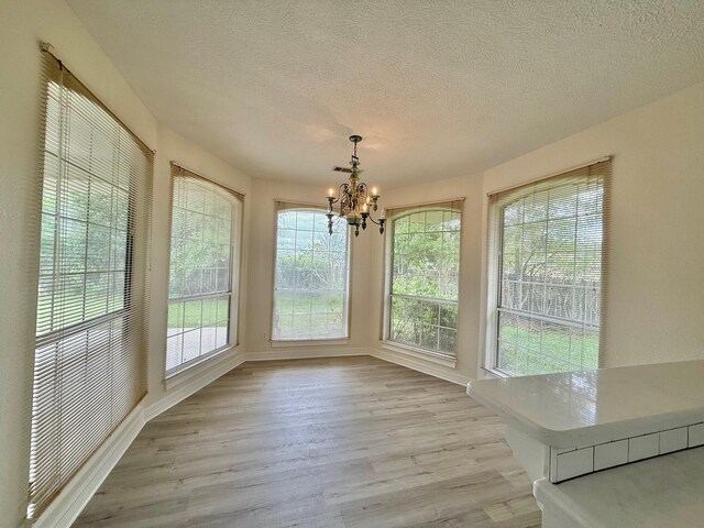 unfurnished sunroom featuring a textured ceiling, wood finished floors, a notable chandelier, and baseboards