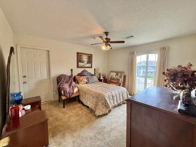 bedroom featuring light carpet, visible vents, a textured ceiling, and a ceiling fan