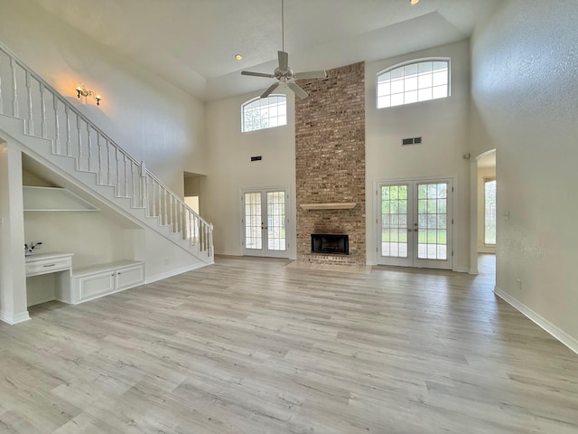 unfurnished living room with baseboards, a brick fireplace, ceiling fan, stairway, and light wood finished floors