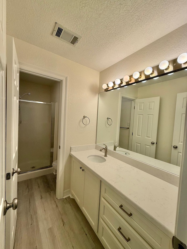 bathroom with vanity, a stall shower, toilet, visible vents, and wood finished floors