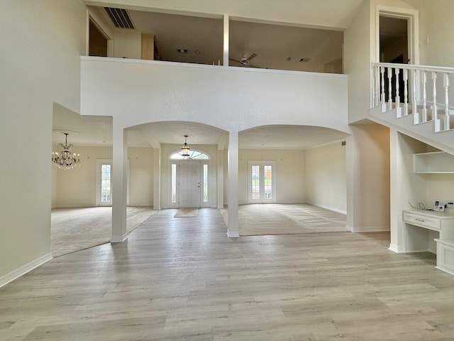 unfurnished living room with light wood finished floors, arched walkways, a towering ceiling, and ceiling fan with notable chandelier