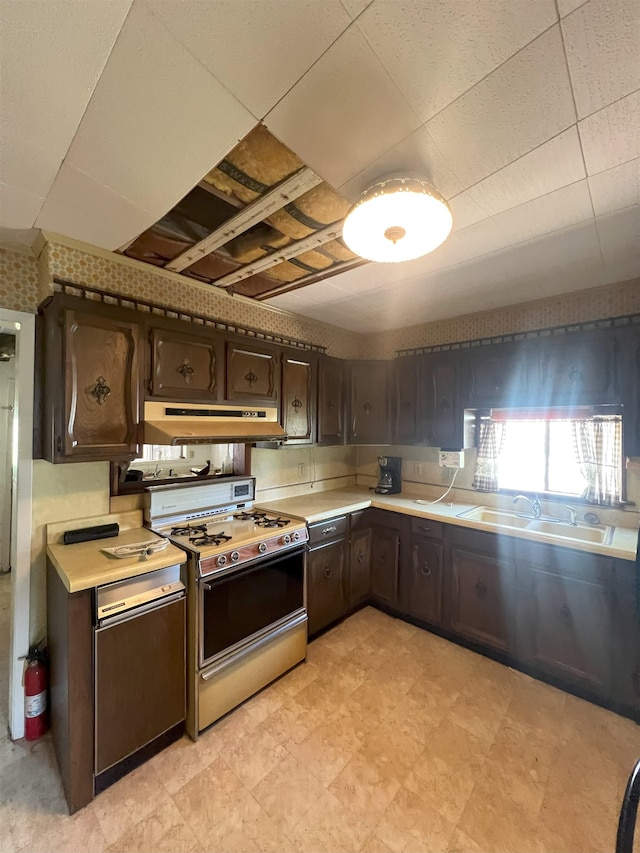 kitchen with light countertops, gas stove, a sink, dark brown cabinets, and under cabinet range hood