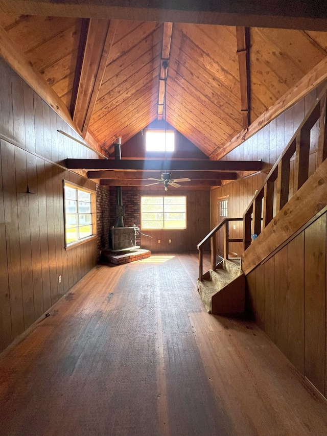 unfurnished living room with a wood stove, hardwood / wood-style flooring, plenty of natural light, and vaulted ceiling with beams