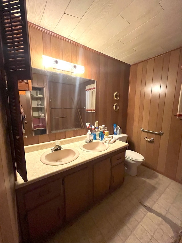 bathroom featuring double vanity, wood walls, a sink, and toilet