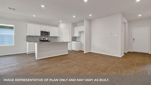 kitchen with hardwood / wood-style floors, a center island with sink, light stone countertops, appliances with stainless steel finishes, and white cabinetry