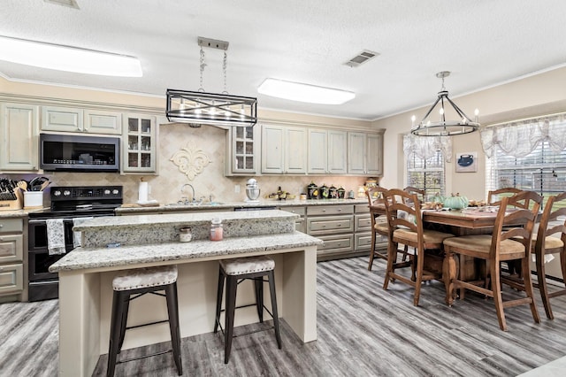 kitchen featuring visible vents, glass insert cabinets, stainless steel microwave, a center island, and black / electric stove