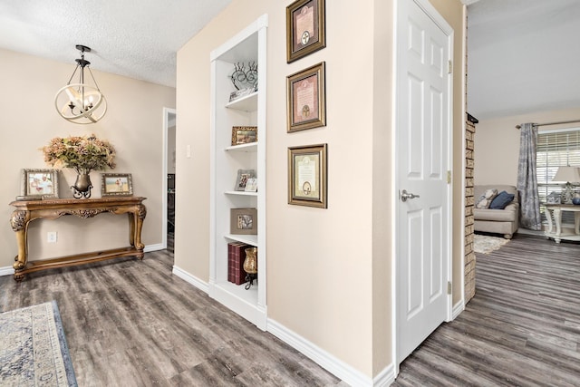 corridor featuring built in shelves, dark wood-style flooring, an inviting chandelier, a textured ceiling, and baseboards