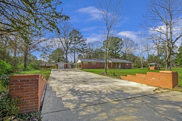 view of front of property featuring a storage shed, a front lawn, concrete driveway, and an outdoor structure