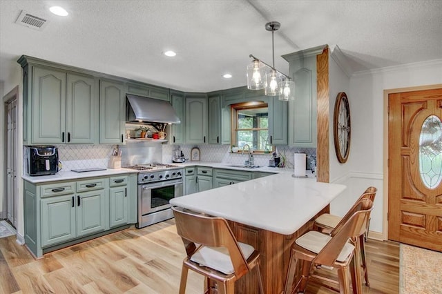 2999 59th St, Port Arthur, TX 77640 - kitchen featuring high end stainless steel range oven, wall chimney exhaust hood, backsplash, light wood finished floors, and green cabinetry