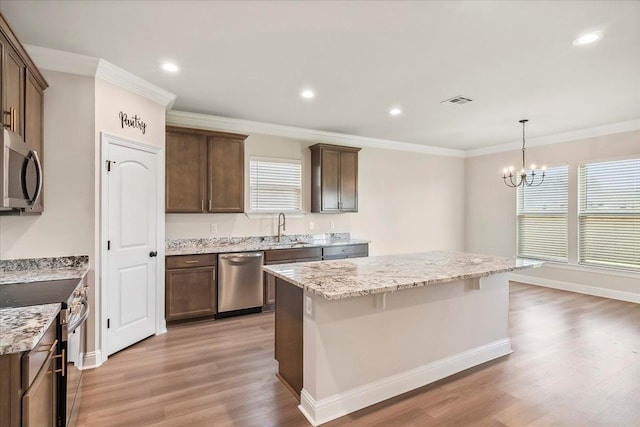 kitchen featuring light stone countertops, a center island, light hardwood / wood-style flooring, appliances with stainless steel finishes, and ornamental molding