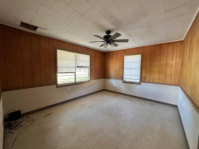 empty room featuring ceiling fan and wood walls