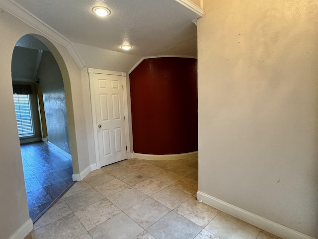 hall featuring light tile patterned flooring, crown molding, lofted ceiling, and a textured ceiling