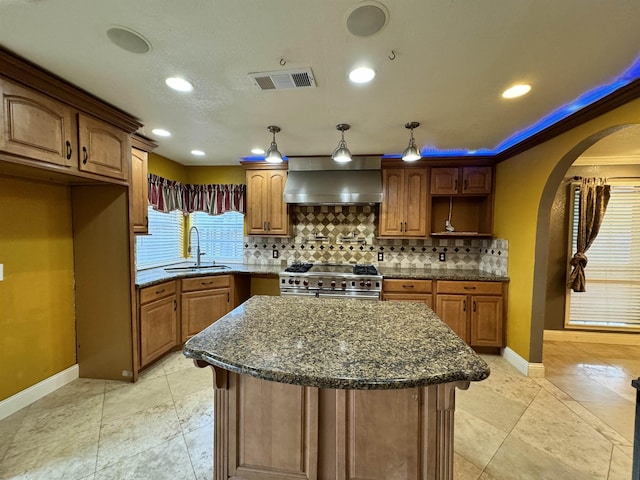 kitchen with dark stone counters, wall chimney exhaust hood, stainless steel range, sink, and a kitchen island