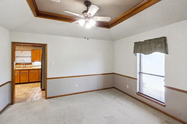 unfurnished room with baseboards, ceiling fan, a sink, a tray ceiling, and light colored carpet