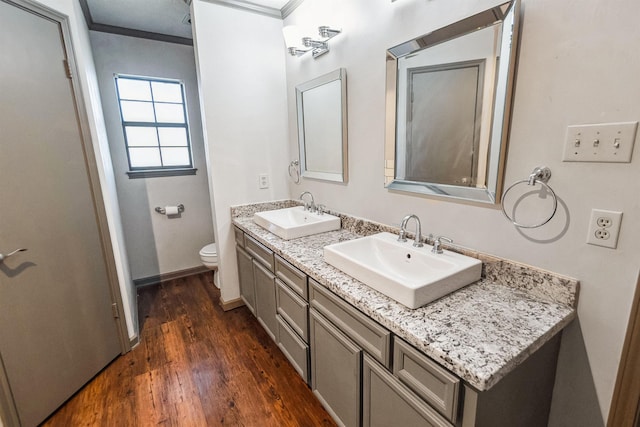 bathroom with toilet, crown molding, wood finished floors, and a sink