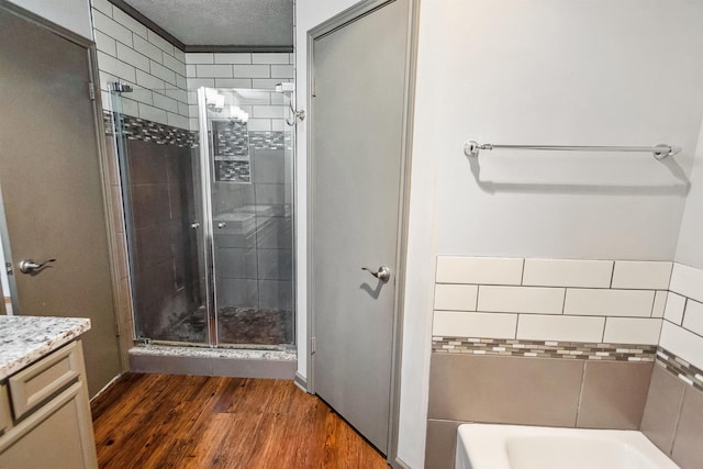 full bathroom featuring wood finished floors, vanity, a textured ceiling, a stall shower, and a bath