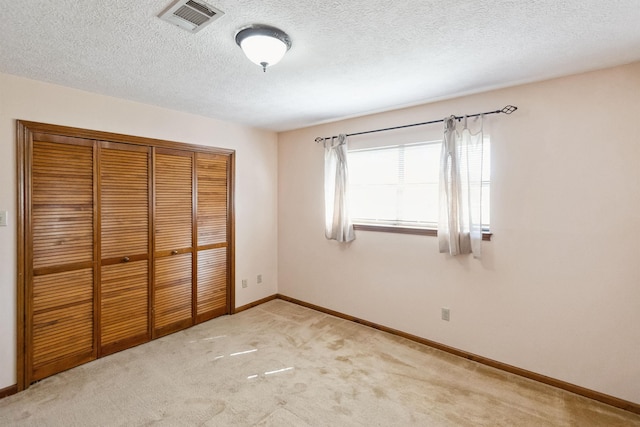 unfurnished bedroom with baseboards, a textured ceiling, visible vents, light carpet, and a closet