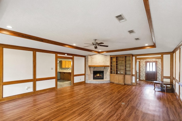 unfurnished living room featuring a textured ceiling, ceiling fan, visible vents, a fireplace, and wood finished floors