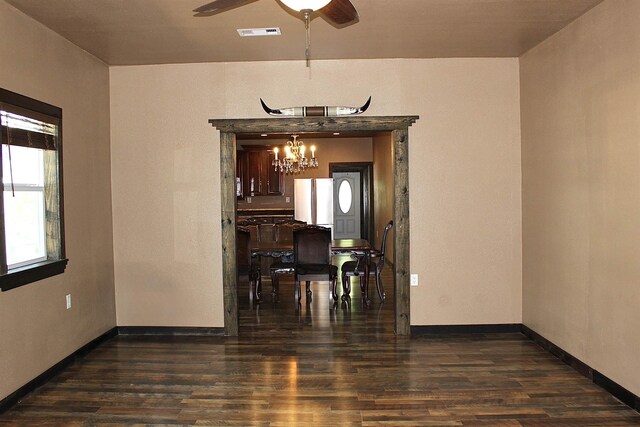 empty room featuring ceiling fan with notable chandelier, baseboards, dark wood finished floors, and visible vents