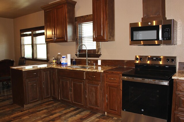 kitchen featuring dark wood finished floors, a peninsula, light stone counters, a sink, and stainless steel appliances