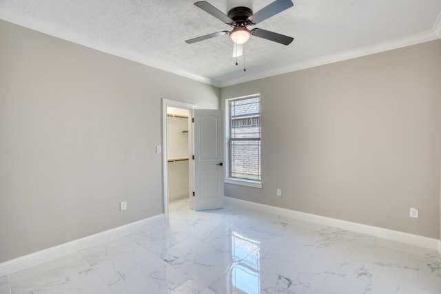 empty room featuring a textured ceiling, marble finish floor, crown molding, and baseboards