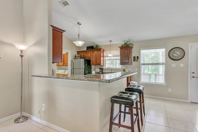 kitchen featuring kitchen peninsula, stainless steel refrigerator, a kitchen breakfast bar, and light stone counters