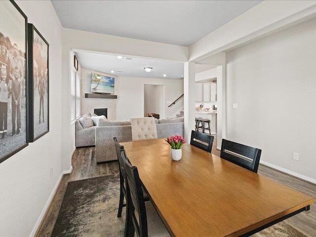 dining space featuring baseboards, dark wood-style flooring, stairs, and a fireplace