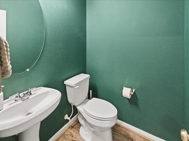 half bathroom featuring toilet, baseboards, a sink, and wood finished floors