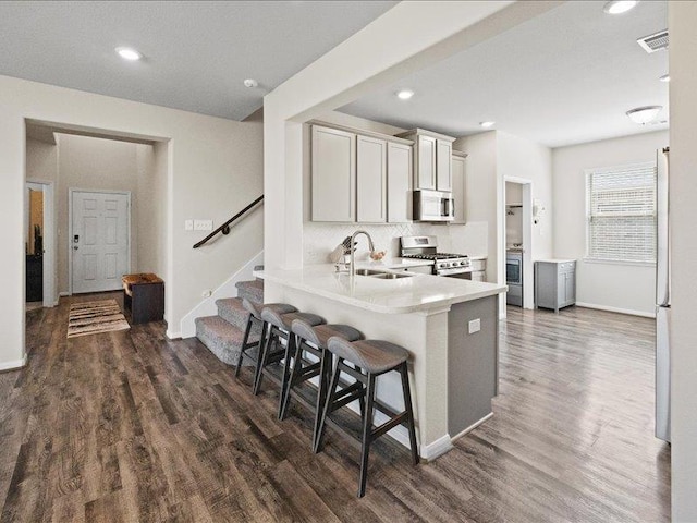 kitchen with a kitchen bar, appliances with stainless steel finishes, a sink, baseboards, and dark wood-type flooring