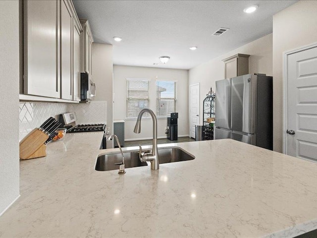 kitchen featuring light stone countertops, a sink, stainless steel appliances, recessed lighting, and backsplash