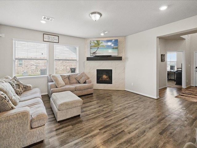 living room with a high end fireplace, baseboards, wood finished floors, and visible vents