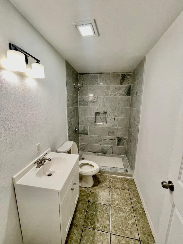 bathroom with a tile shower, vanity, and toilet