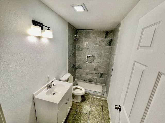 bathroom with tiled shower, vanity, and toilet