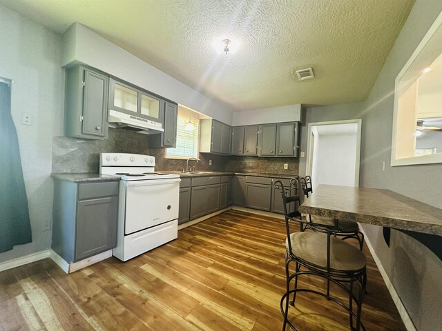 2922 Little Cypress Dr, Orange, TX 77632 - kitchen featuring white range with electric cooktop, under cabinet range hood, gray cabinetry, dark wood-style flooring, and a textured ceiling