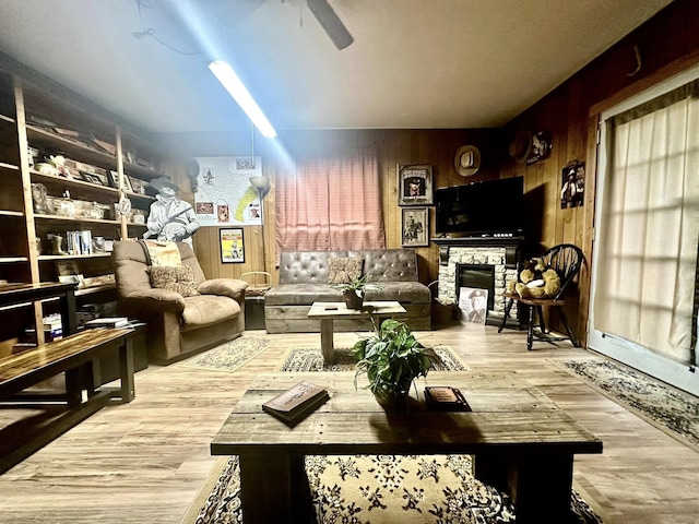 interior space with ceiling fan, light wood-type flooring, a fireplace, and wooden walls