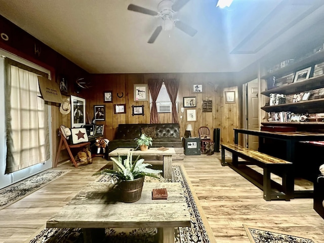 living room featuring ceiling fan, light wood-type flooring, and wood walls