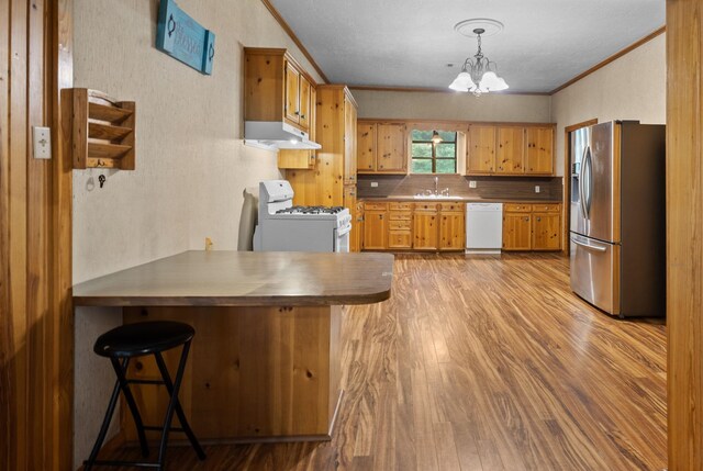 10425 Bussey Rd, Silsbee, TX 77656 - kitchen featuring white appliances, under cabinet range hood, ornamental molding, light wood-style flooring, and a peninsula