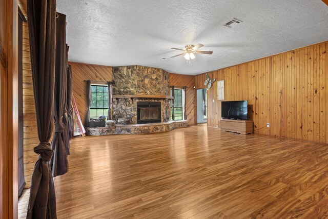 10425 Bussey Rd, Silsbee, TX 77656 - unfurnished living room featuring wooden walls, ceiling fan, a textured ceiling, wood finished floors, and a stone fireplace