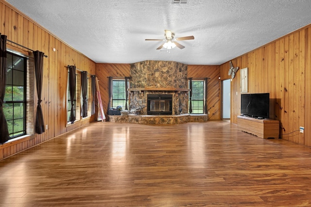 10425 Bussey Rd, Silsbee, TX 77656 - unfurnished living room with wooden walls, wood finished floors, ceiling fan, a textured ceiling, and a fireplace