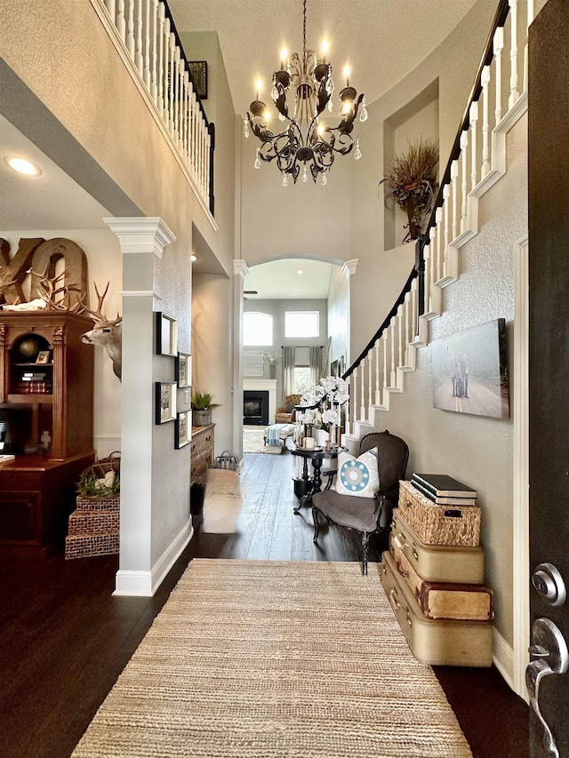 foyer entrance with ornate columns, dark hardwood / wood-style flooring, a towering ceiling, and an inviting chandelier