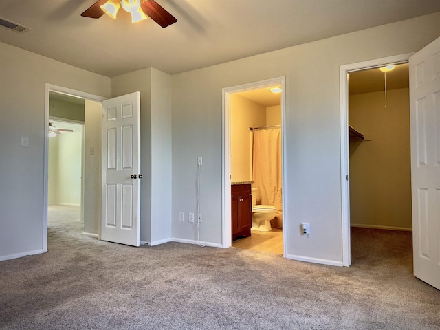 unfurnished bedroom with connected bathroom, ceiling fan, a walk in closet, light carpet, and a closet