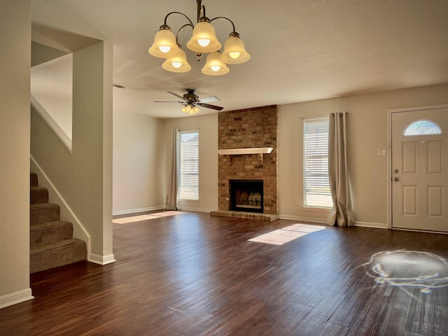 unfurnished living room with ceiling fan with notable chandelier, dark hardwood / wood-style floors, and a brick fireplace